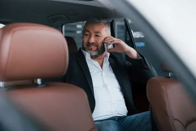 Man in a suit on a phone in a car, brown seats, looking at the side.