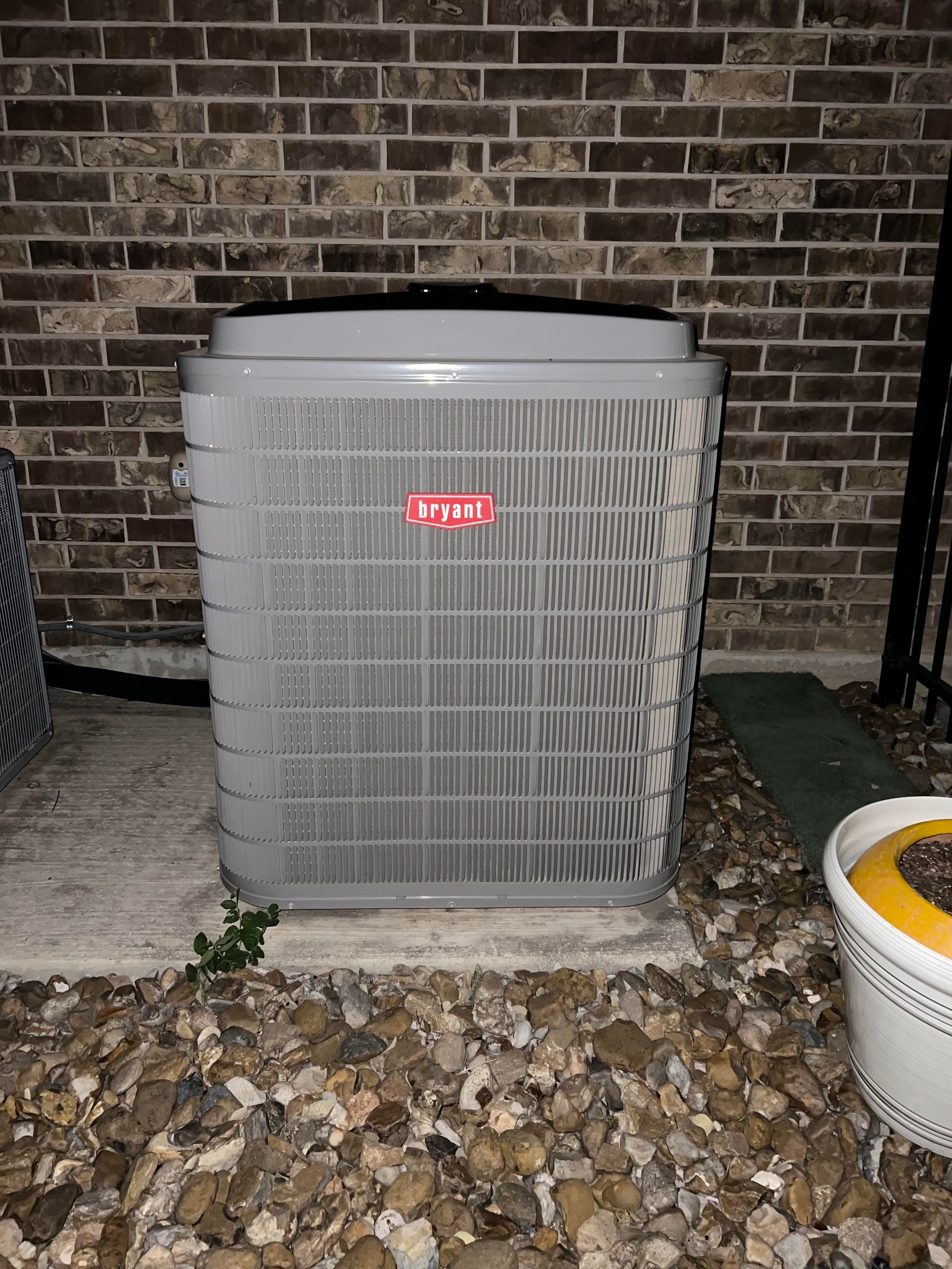 Gray Bryant air conditioning unit outside on gravel next to a brick wall.