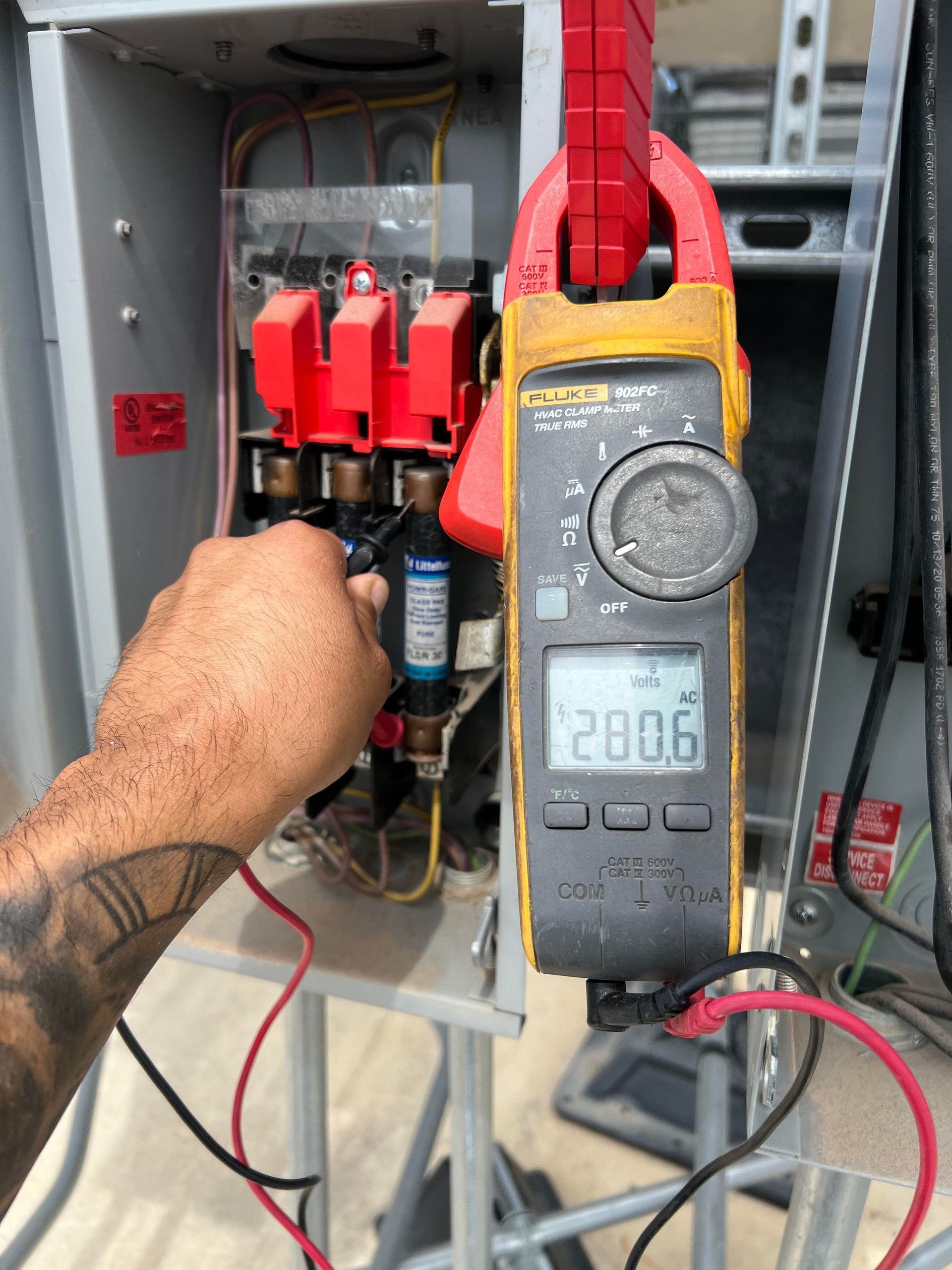 Electrical worker using a clamp meter to measure current in a fuse box, reading 280.6.