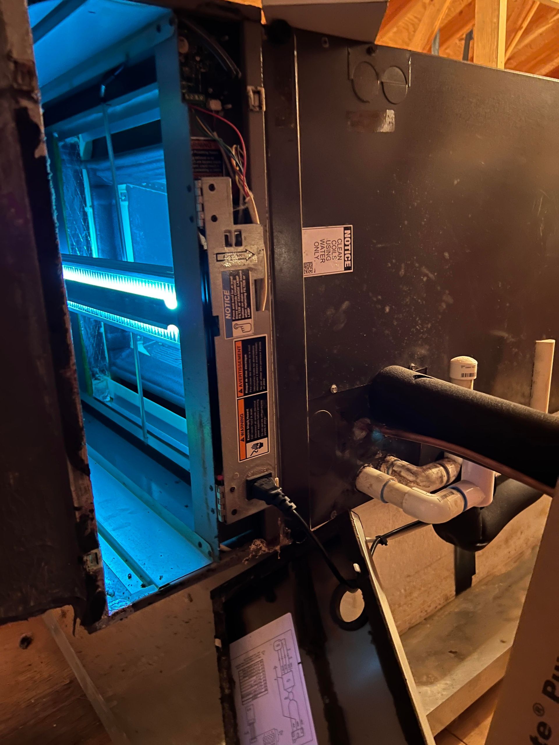 HVAC unit with blue UV light. Open panel shows internal components. Plumbing visible.