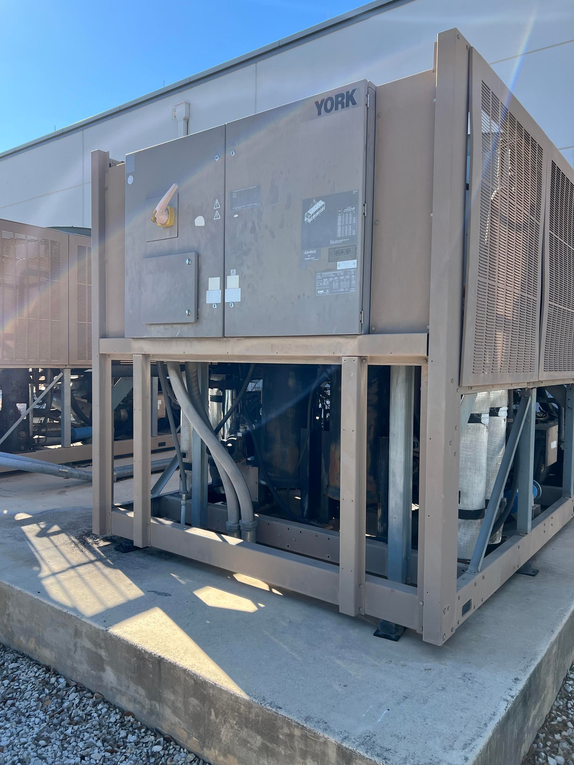 A beige York industrial chiller unit on a concrete pad with a light-colored building in the background.