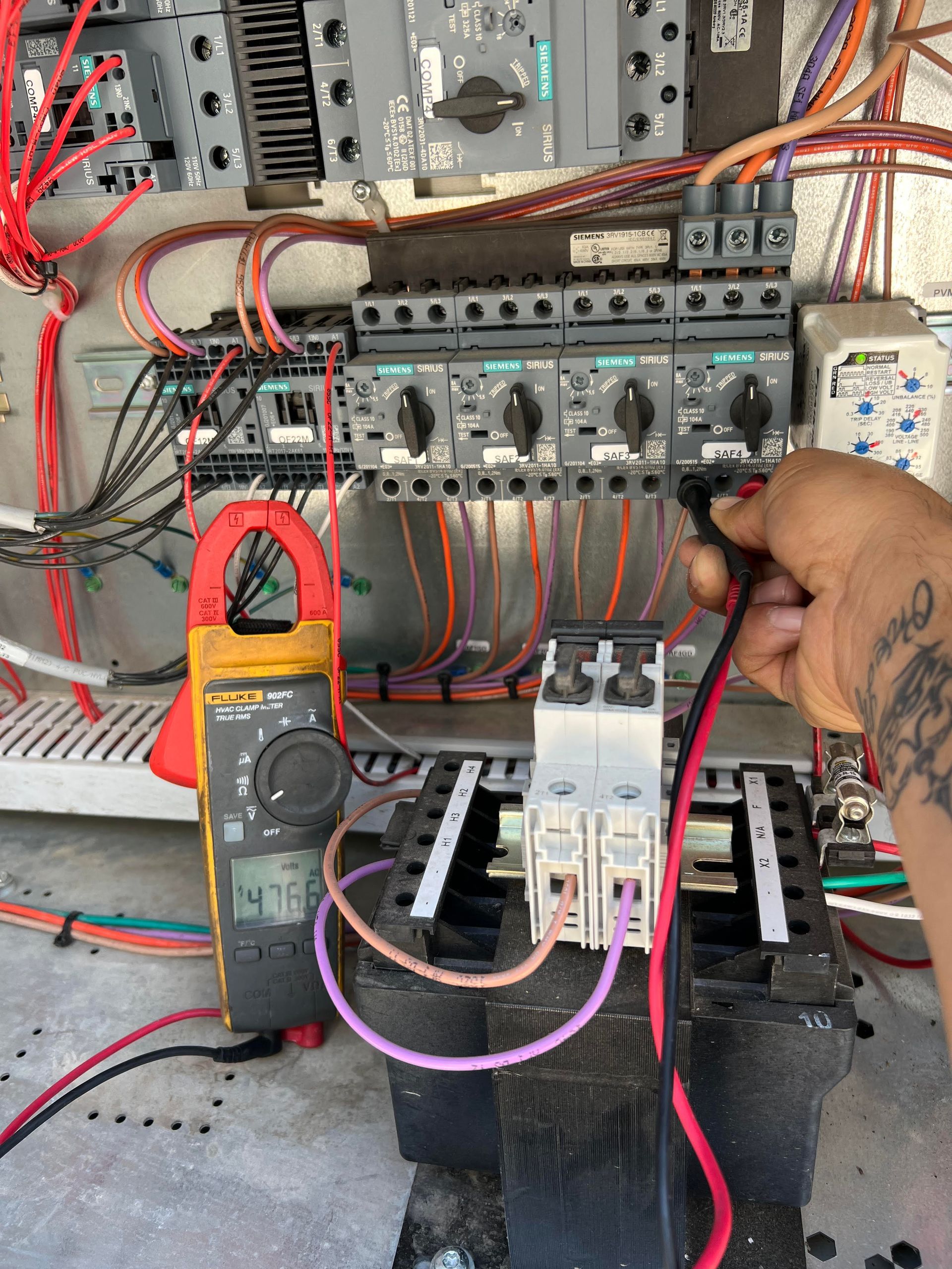 Person testing electrical panel with a multimeter. Black and red wires, switches, and a digital display.