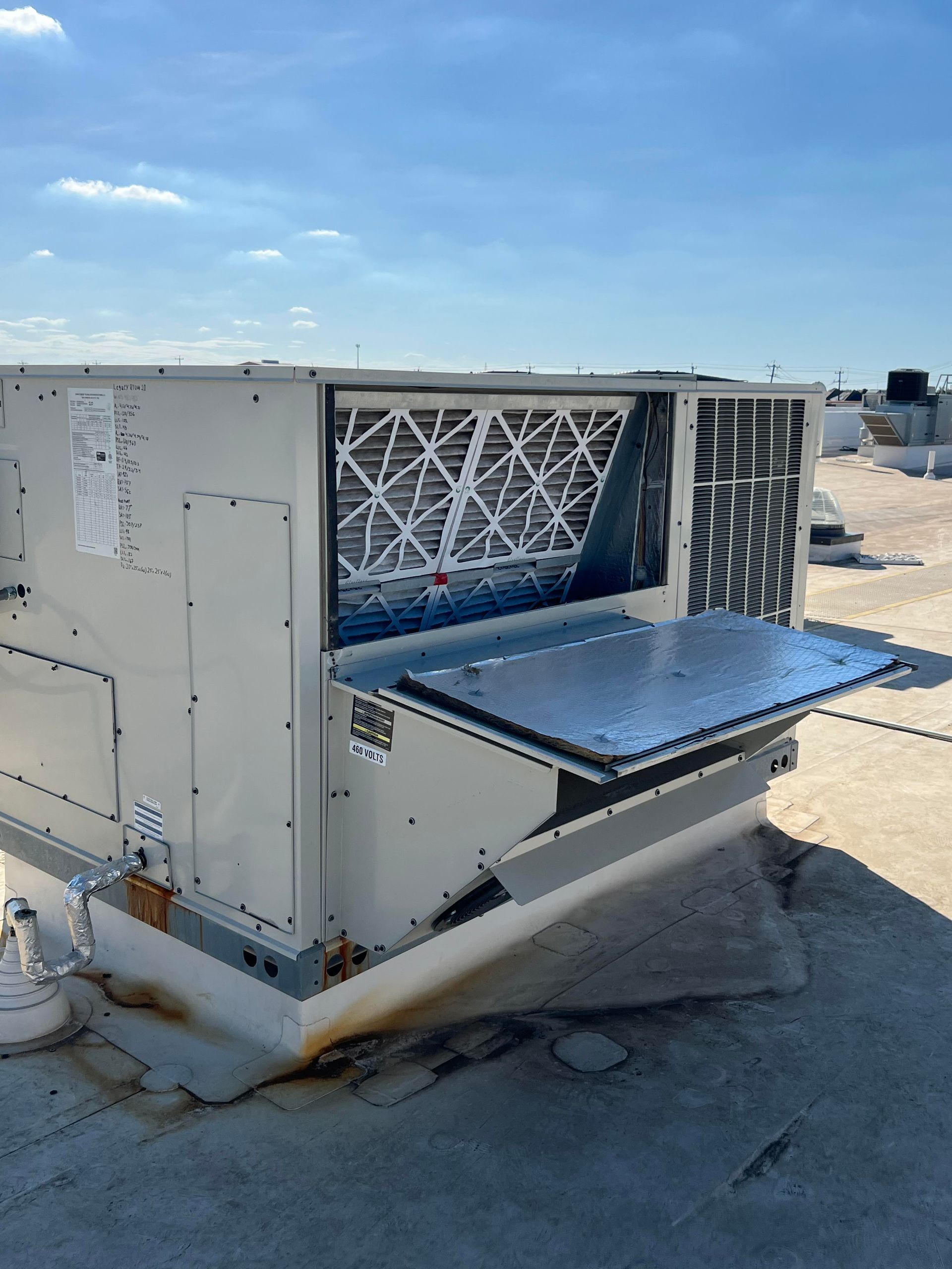 Rooftop HVAC unit with open access panel, showing air filter, against a blue sky.