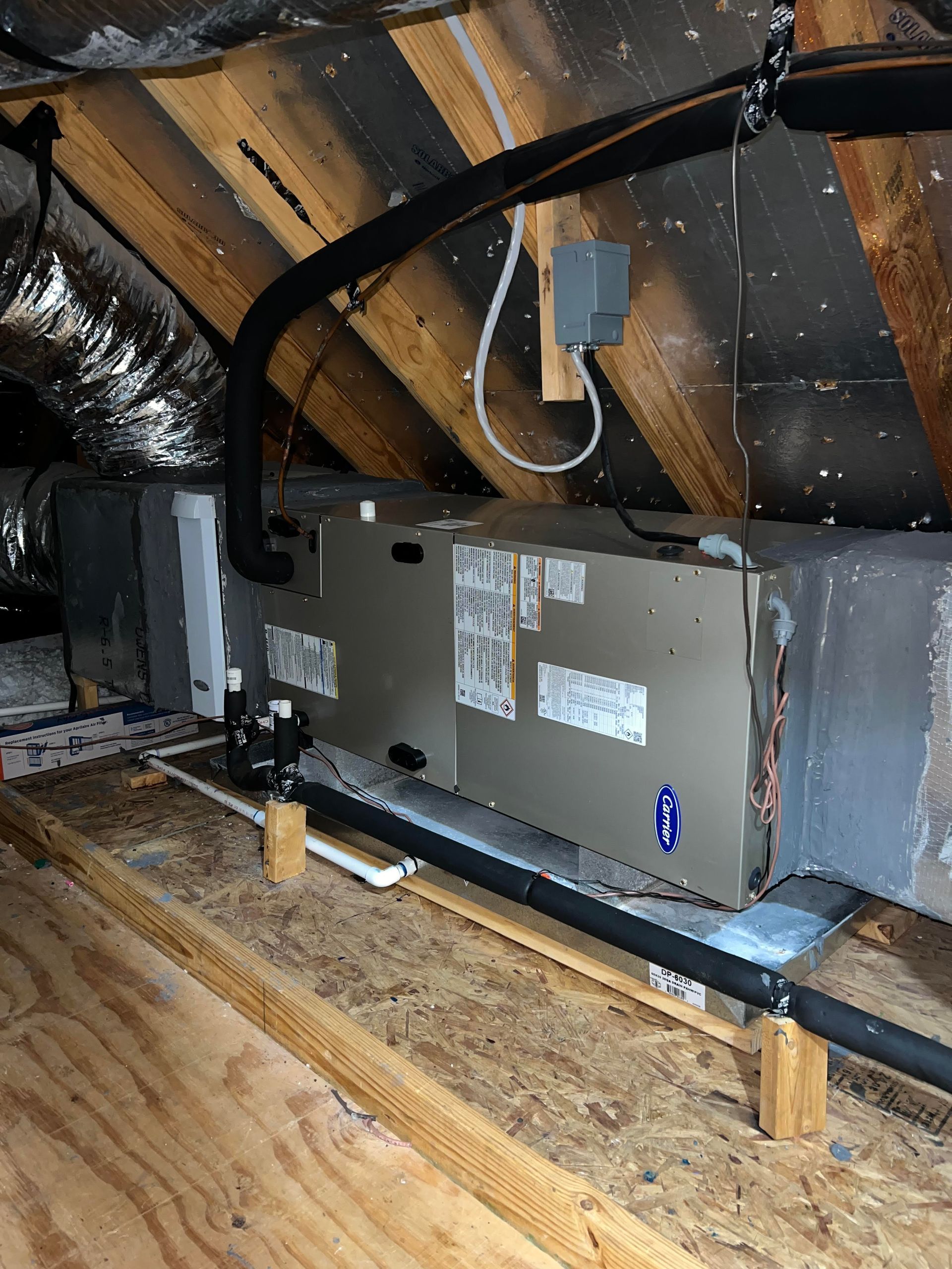 HVAC unit in an attic with insulated black pipes and a gray electrical box.