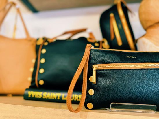 Close-up of leather handbags in various styles and colors, with gold hardware and a book.