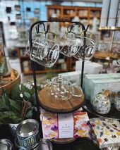 Glass teacups and teapot on a metal stand displayed in a store. Cork base, tea boxes, and greenery.
