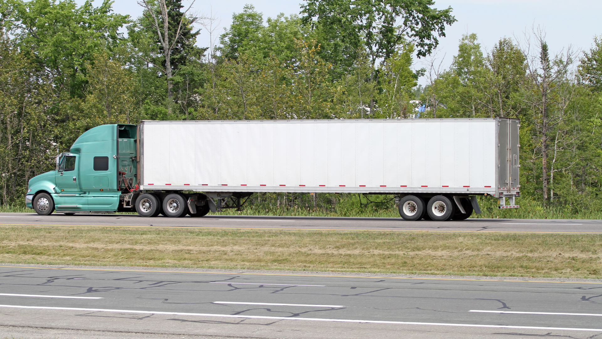 A green semi truck with a white trailer is driving down a highway.