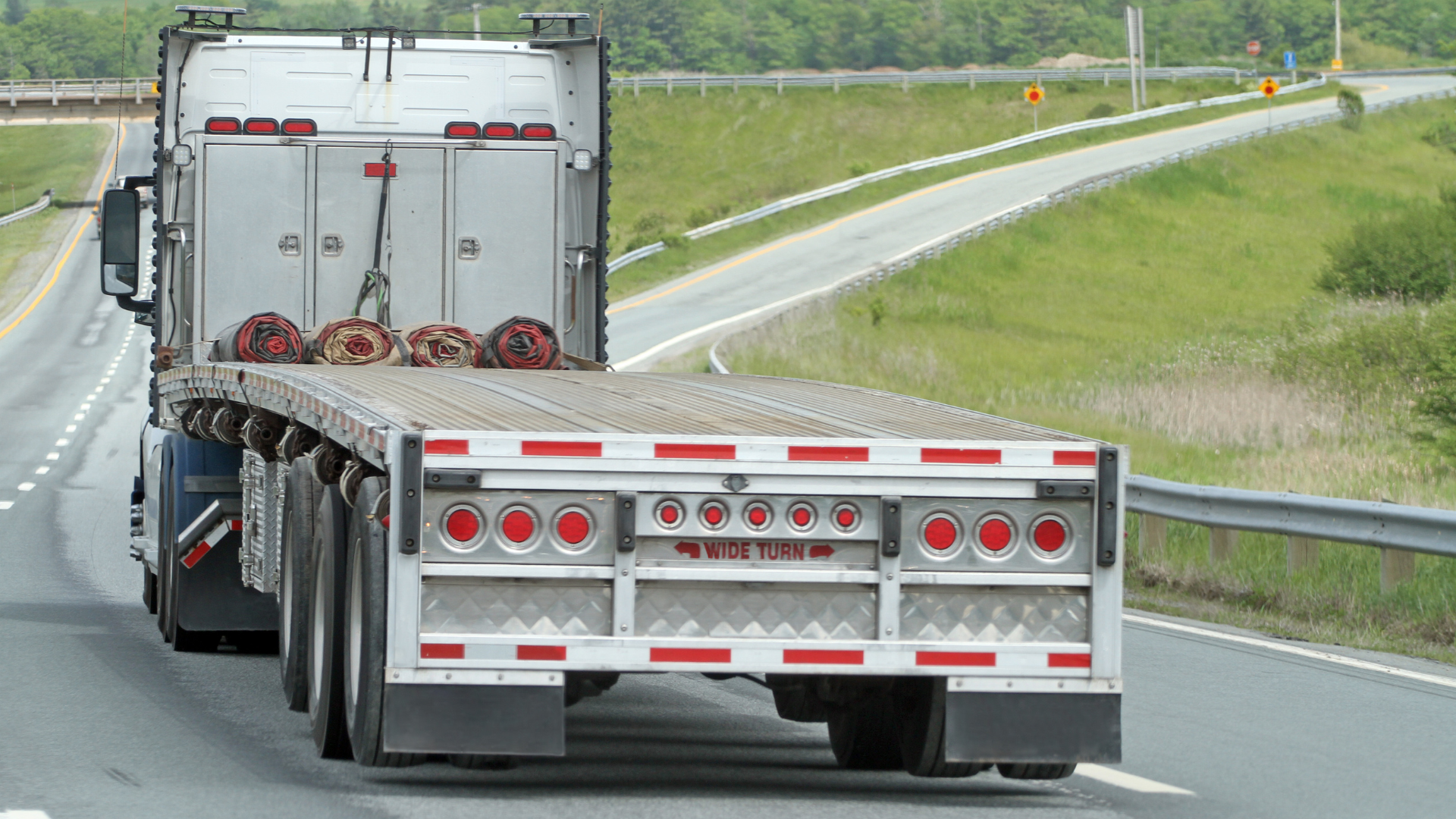 A semi truck with a flat bed is driving down a highway.
