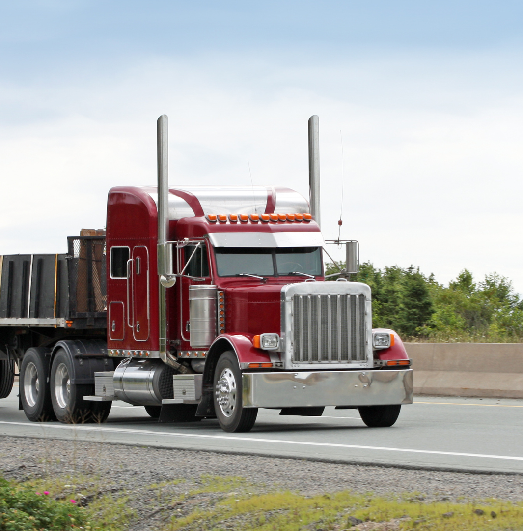A red semi truck is driving down a highway.