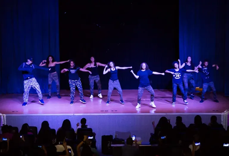 Um grupo de pessoas está dançando em um palco na frente de uma multidão.