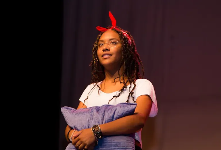 Uma mulher está segurando uma almofada roxa no palco.