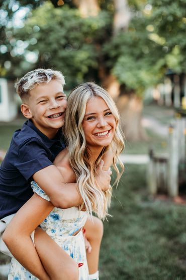Boy with braces gives a piggyback ride to a smiling woman in a garden setting.