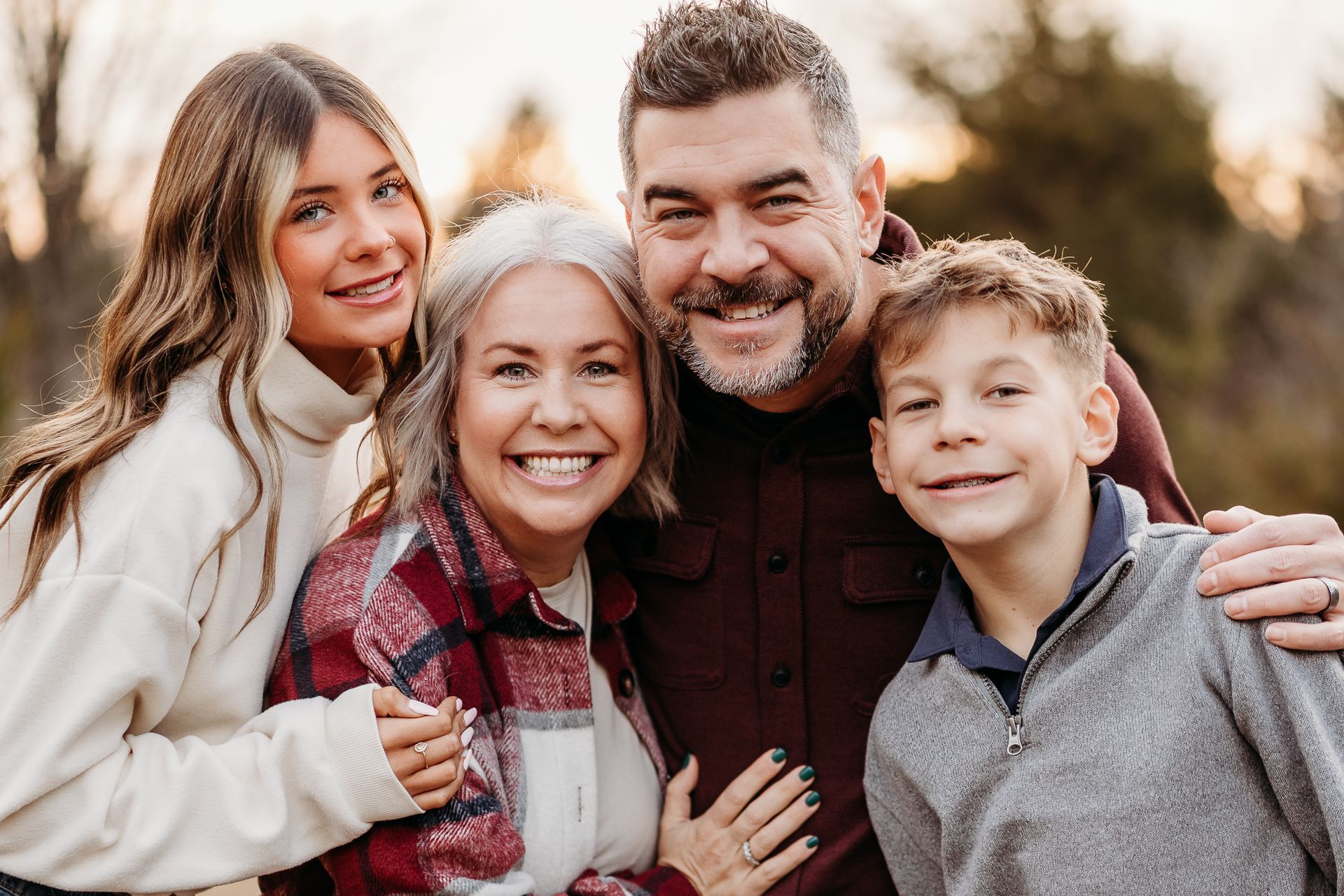 Family of four smiling outdoors: two adults and two children.