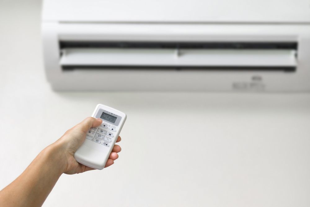 Hand Holding Remote, Pointing It at a Wall-mounted Air Conditioner — RedJak Air Conditioning Services in Logan, QLD