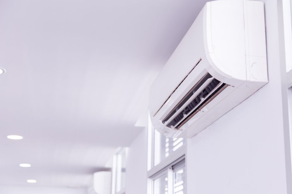 White wall-mounted air conditioner unit in a bright, white room with recessed lighting and a window.