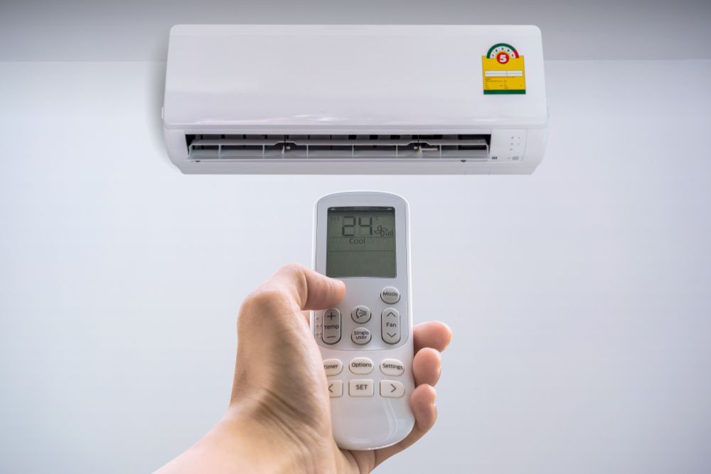 Hand holding remote control adjusting wall-mounted air conditioner; white setting. — RedJak Air Conditioning Services in Logan, QLD