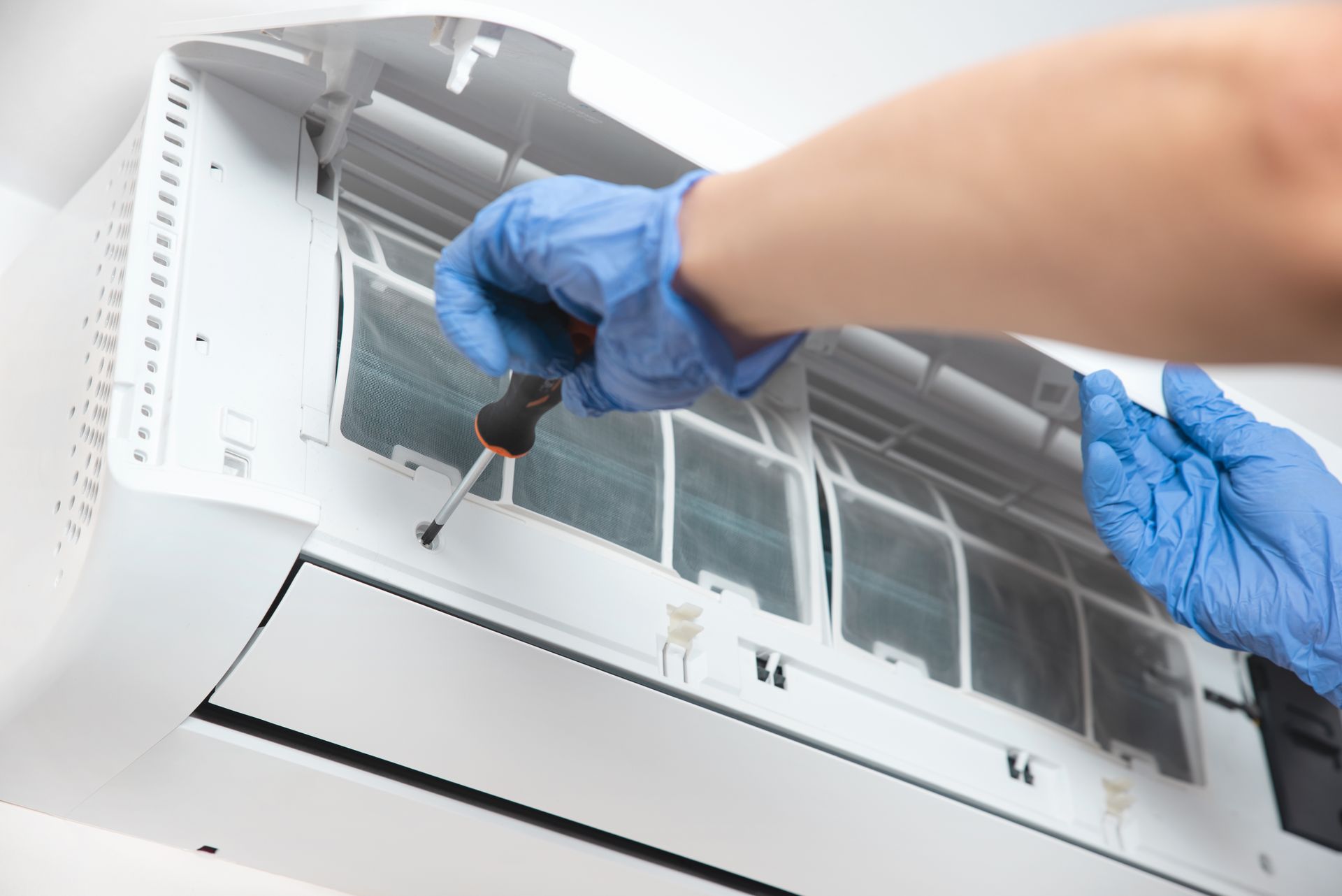 Person in Blue Gloves Using a Screwdriver on an Air Conditioner Unit — RedJak Air Conditioning Services in Willawong, QLD