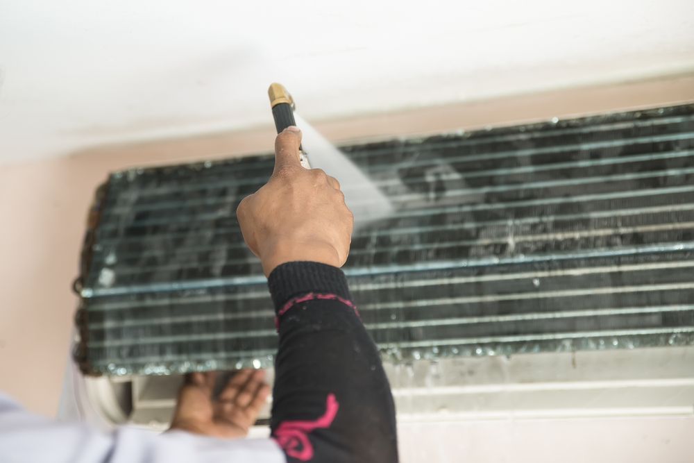 Person Spraying an Air Conditioner Coil With a Hose, Cleaning It — RedJak Air Conditioning Services in Willawong, QLD