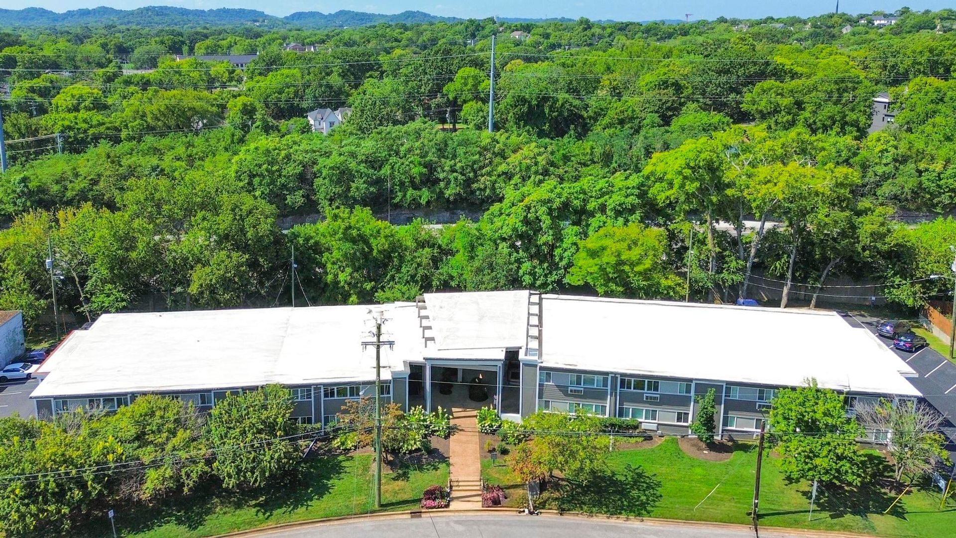 Aerial view of a white-roofed building surrounded by dense green trees and landscaped grounds.