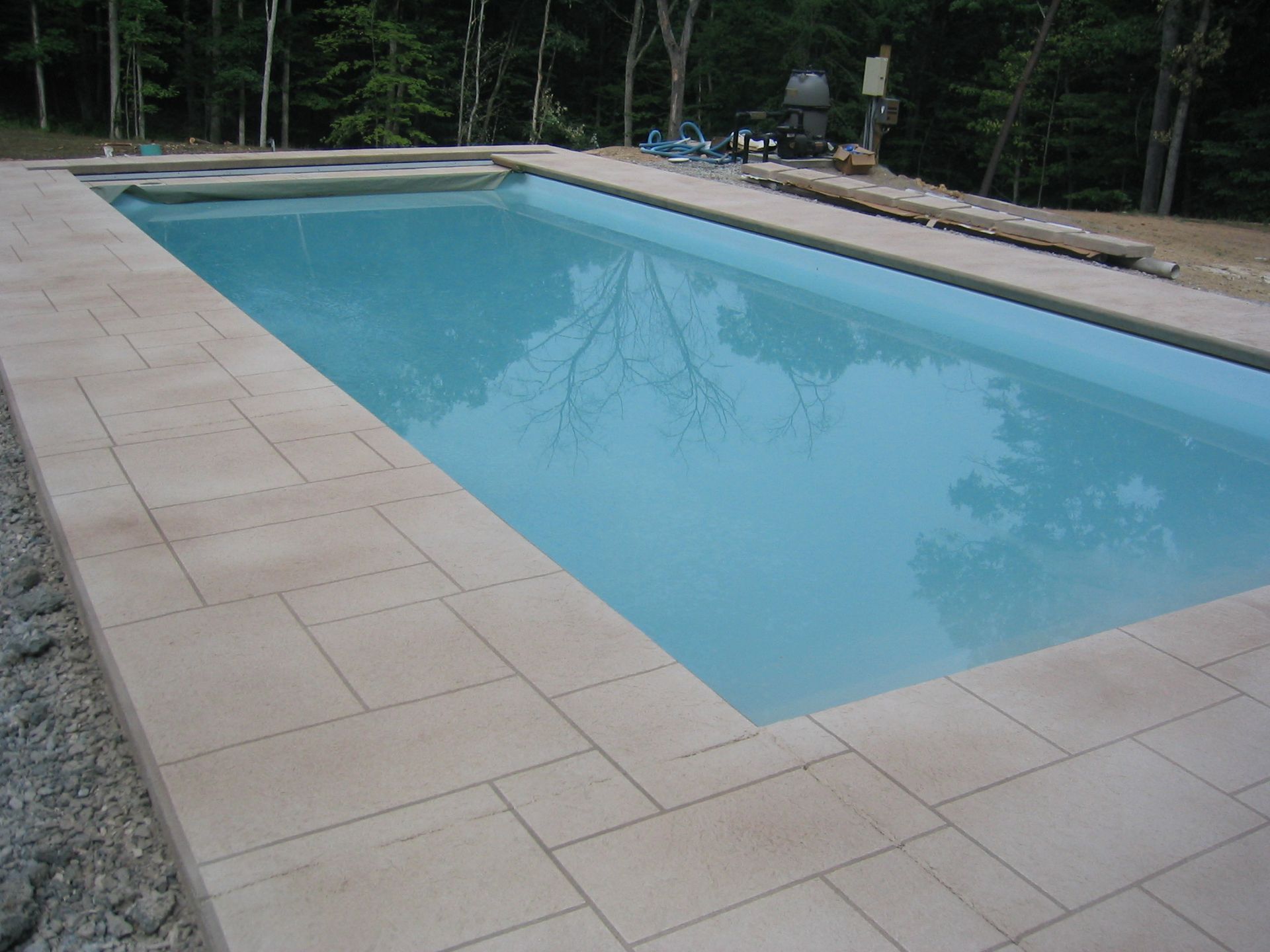 Rectangular swimming pool with light-colored stone border, surrounded by trees.