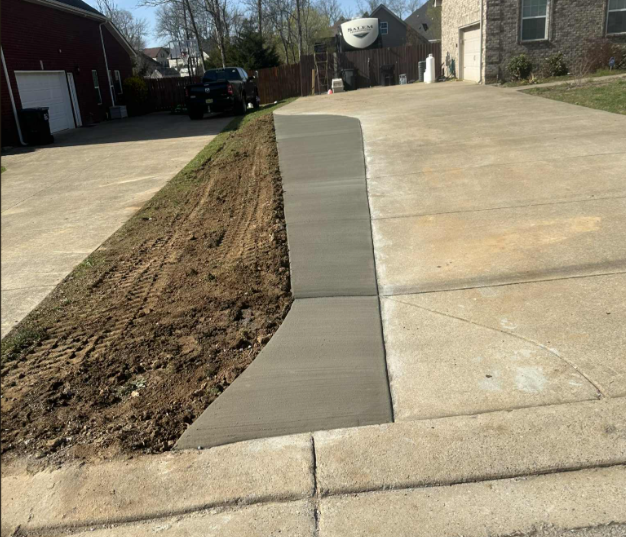 Concrete walkway with gray gravel separating the squares, running alongside a light-colored house.