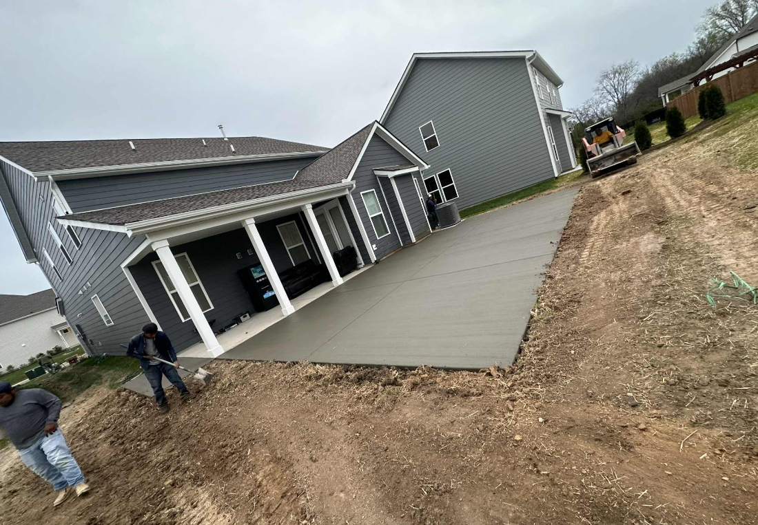 Concrete driveway leading to a dark blue house with a white garage door. Sunny day.