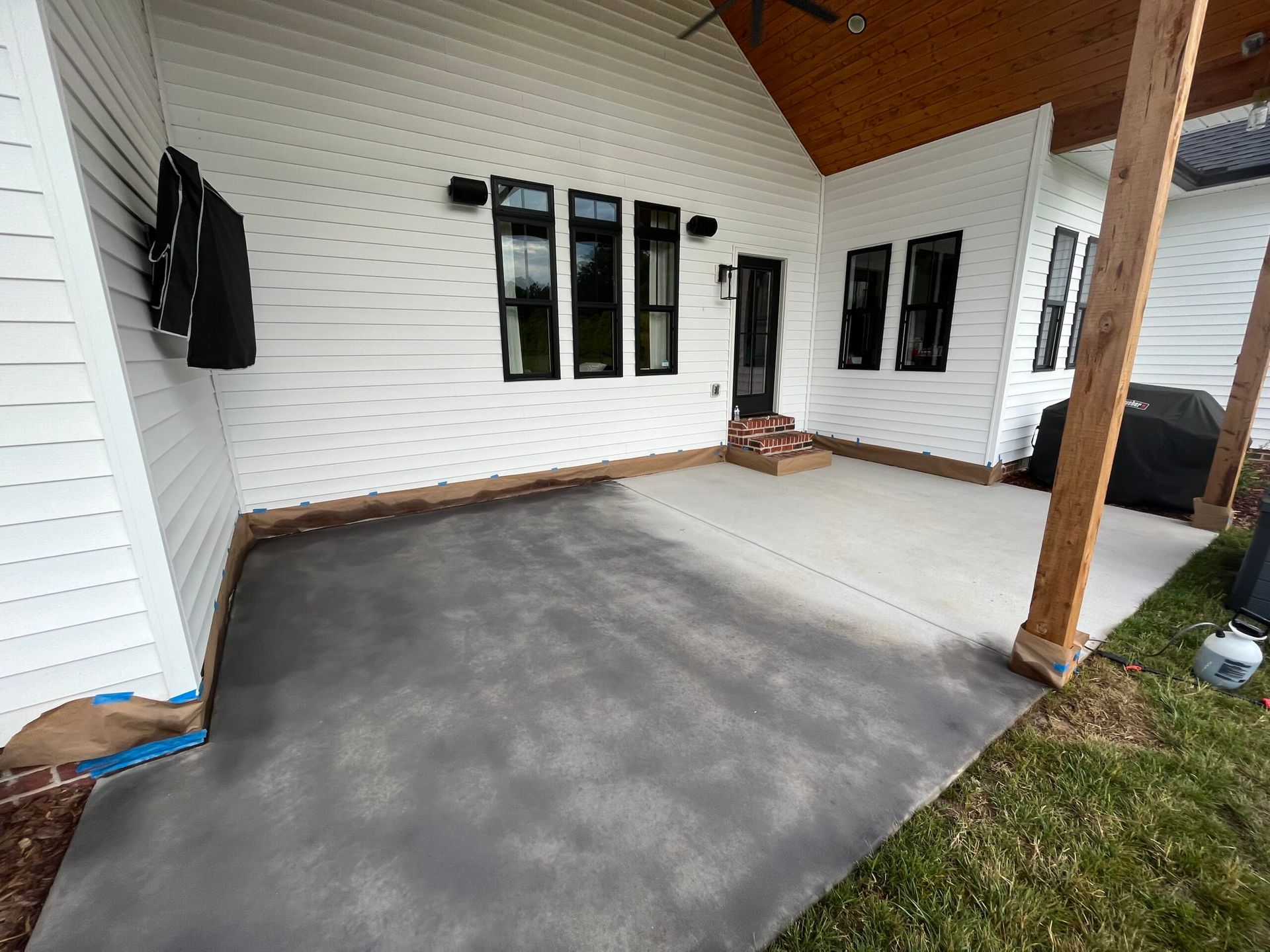 Covered patio with gray concrete floor, white siding, and black-framed windows.