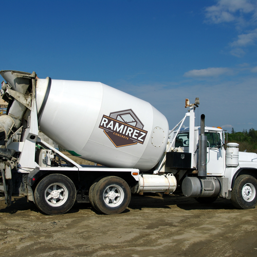 White Ramirez cement mixer truck on a construction site under a blue sky.