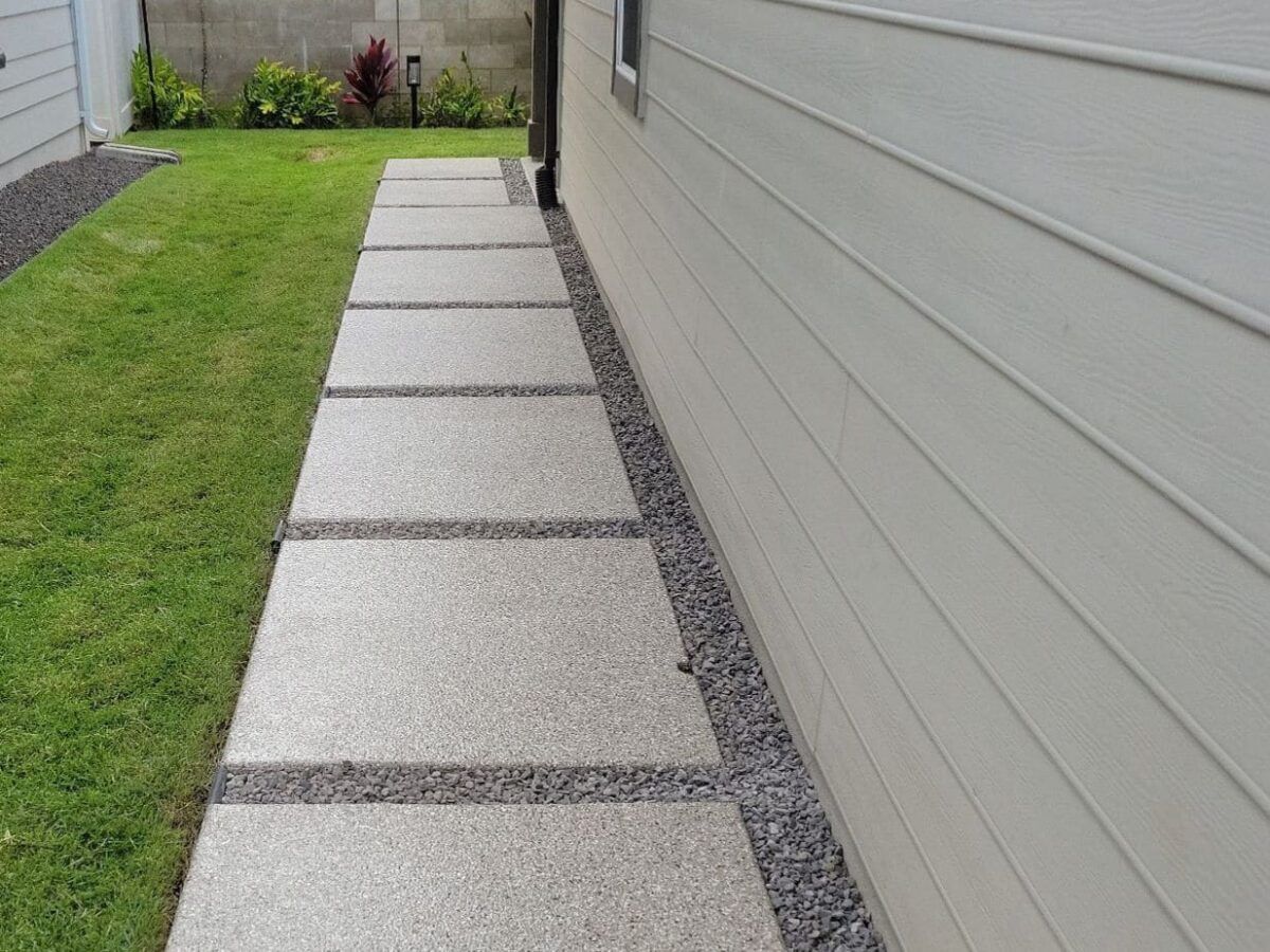Concrete walkway with gray gravel separating the squares, running alongside a light-colored house.