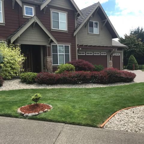 Suburban house with manicured lawn, red shrubs, and a concrete walkway under a partly cloudy sky