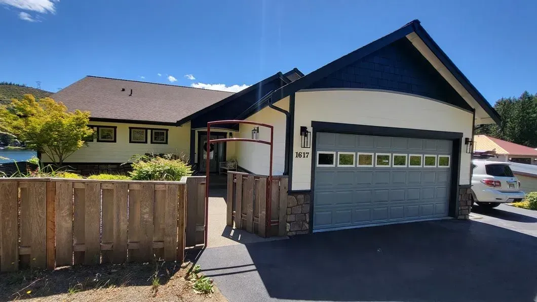 Suburban house with tan siding, dark roof, and gray garage door behind a wooden fence