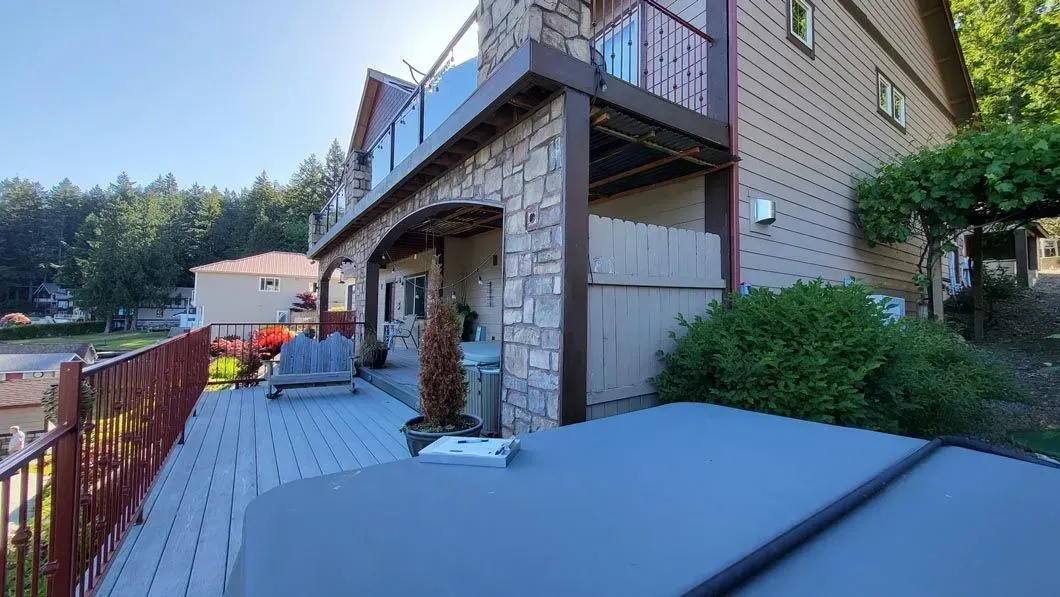 Backyard patio beside a brick house with a deck, railing, and a view of trees and water at sunset