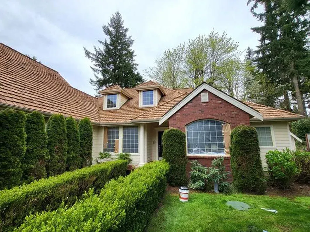 Cottage with red-tile roof, brick front, tall hedges, and a green lawn in a wooded garden.