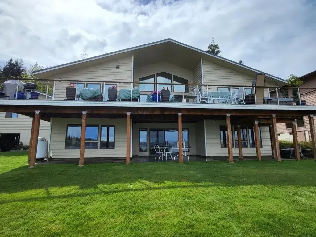 Two-story house with a covered deck and grassy backyard on a cloudy day