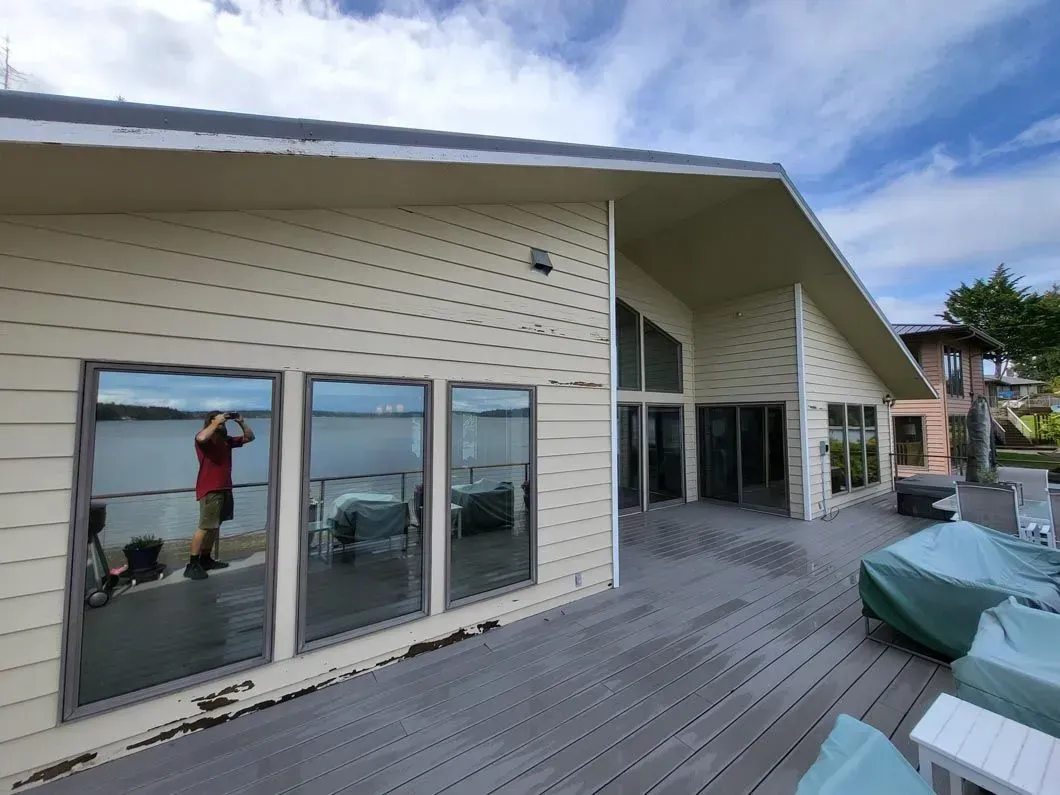 Exterior of a beige house with a wooden deck, sliding glass doors, and patio furniture under a cloudy sky