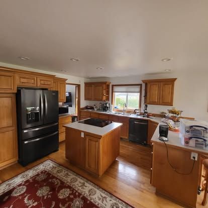 Bright kitchen with wood cabinets, black appliances, central island, and a window over the sink