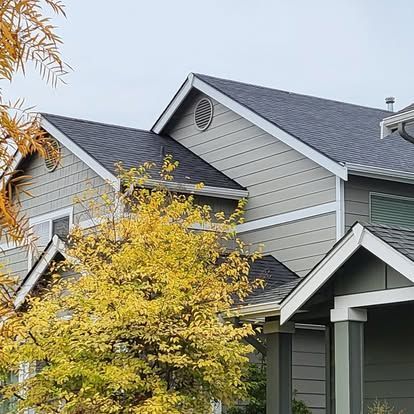 Suburban house with gray siding, dark roof, and a yellow autumn tree in front