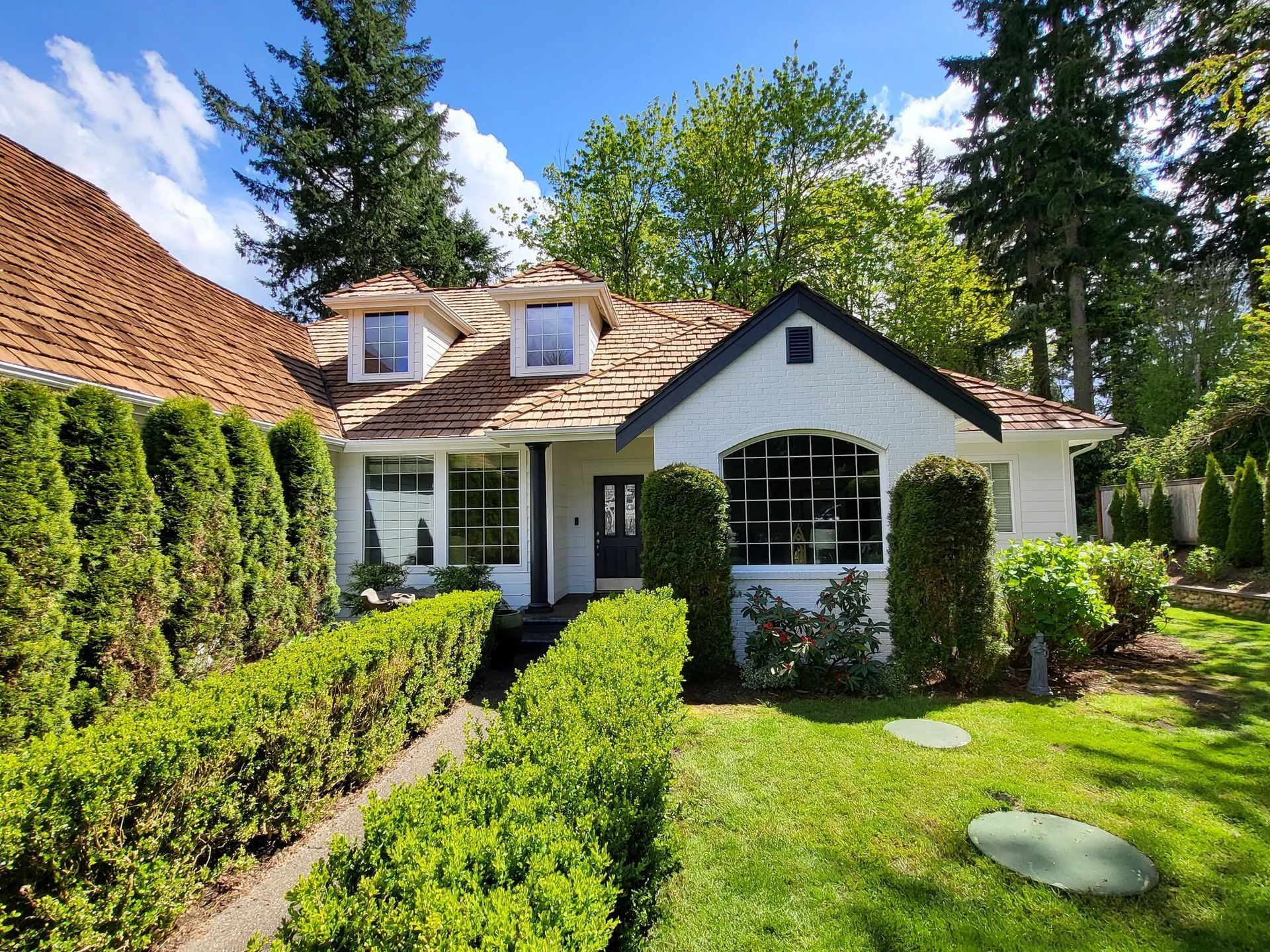 White cottage with green hedges and a manicured lawn in a sunny garden