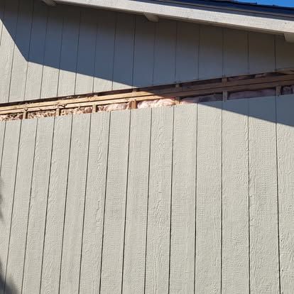 Close-up of a gray exterior wall with damaged trim and exposed wood under the roofline.