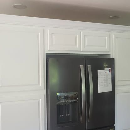 Black stainless steel refrigerator with water dispenser, framed by white kitchen cabinets
