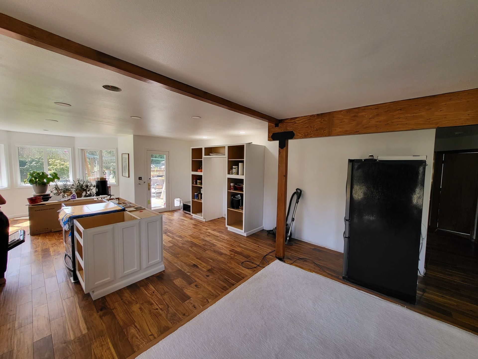 Bright open kitchen and living room with wood floors, white cabinets, and large windows.