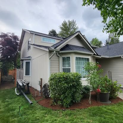 Small beige house with white trim, front shrubs, and a cloudy sky over a green lawn.