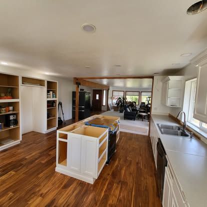 Bright kitchen with white cabinets, wood floors, central island, and open view to living room.