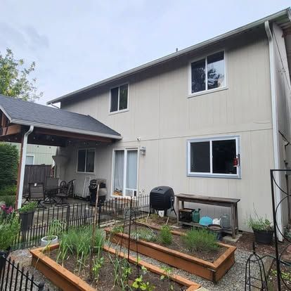 Backyard garden with raised beds beside a beige two-story house and covered patio