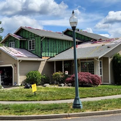 Suburban house under repair with green siding, exposed roof, and a streetlamp in front