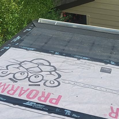 Partially installed roof underlayment with cartoon-like black outline and pink lettering, seen near green trees