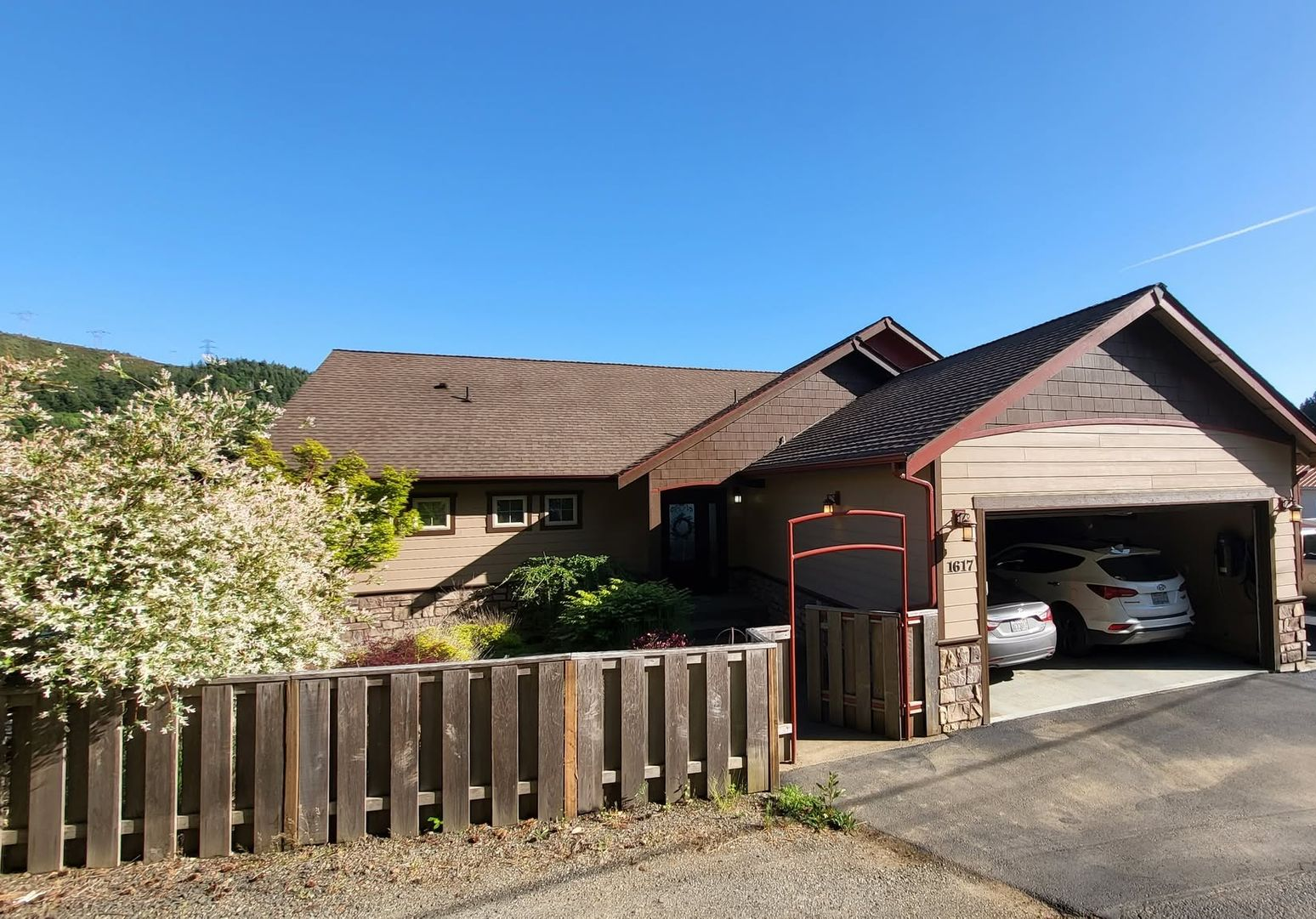 Suburban house with open garage, parked cars, and a wooden fence under a clear blue sky