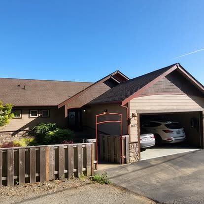 Suburban house with open garage, parked cars, and wooden front fence under a clear blue sky