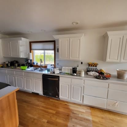 Bright kitchen with white cabinets, wood floor, and a window over the sink; counters are cluttered.