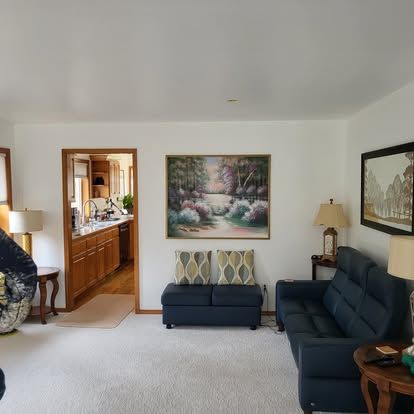 Bright living room with white walls, navy sofas, lamps, and a doorway to a kitchen area
